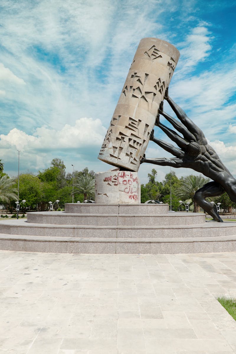 Vandalized sculpture in a Baghdad park under a vibrant blue sky.